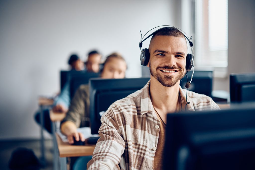 Happy student attending computer class and looking at camera.